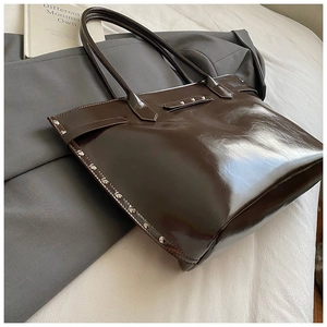Detail of dark brown glossy patent leather tote bag with silver rivet studs on sides
