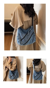 Detail view of washed denim shoulder bag with multiple zippers and wide strap design