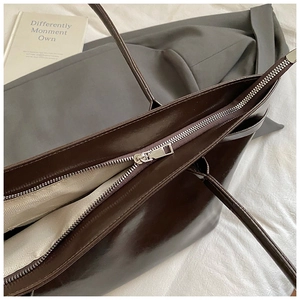 Detail of deep brown glossy leather tote with silver zipper and herringbone lining