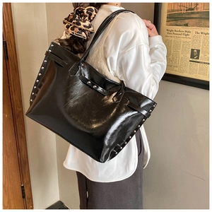 Detail of large black glossy tote bag with silver rivets and vintage commuter style