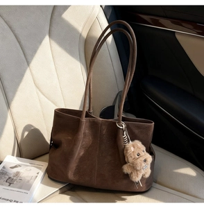 Detail of a brown suede tote bag with long handles and a cute plush puppy charm on a car seat