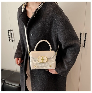Detailed view of woven leather mini handbag with gold clasp on tweed coat