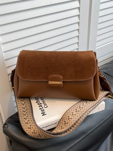 Brown leather crossbody bag with ethnic patterned strap on a white book surface