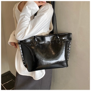 Detail of glossy black leather tote bag with silver studs and thin shoulder straps