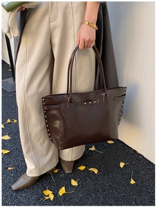 Detail of dark brown tote bag with silver studs and oily leather texture in autumn setting