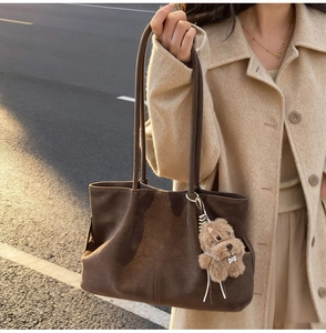 Detail of a large dark brown suede tote bag with a cute plush dog charm on street