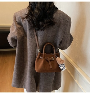 Brown suede bucket bag with decorative buckle and cute bear charm shown on model