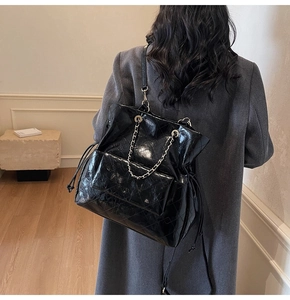 Detail of black quilted patent leather tote bag with silver chain strap and drawstring design