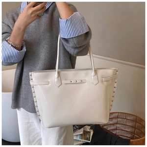 Detail view of cream-colored oversized tote bag with polished finish and silver rivet studs