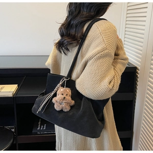 Detail of black suede tote bag with brown plush puppy charm and striped tassel accent