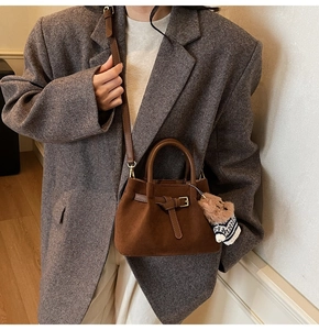 Brown faux suede bucket bag shown with adjustable strap and cute bear charm on a model