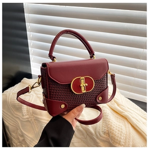 Close-up of deep red woven crossbody bag with gold buckle and adjustable strap