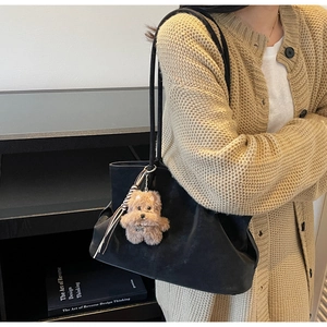 Detail view of large black suede tote bag with cute plush puppy charm and ribbon