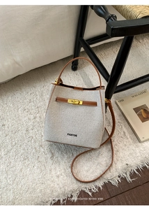 Detail of PANTOR bucket bag featuring ivory canvas with brown leather trim and gold twist lock