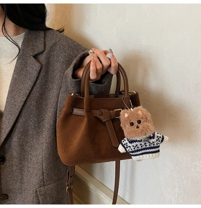 Detail of dark brown suede bucket bag with leather handle and plush bear charm