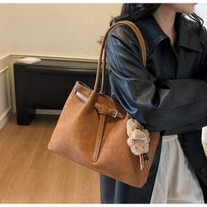 Detail of a brown woven tote bag with adjustable straps and a plush bear charm detail