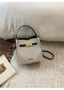 Detail of woven bucket bag with black leather trim and golden twist lock closure