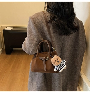 Detail view of a vintage dark brown suede bucket bag with a cute plush bear charm