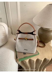 Detail of beige canvas and brown leather bucket bag with gold lock on a wooden desk