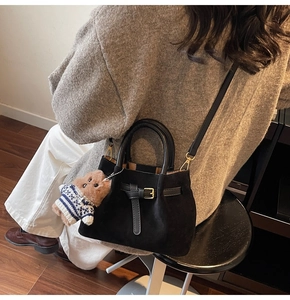 Detail of a black suede bucket bag featuring a belt buckle clasp and a small bear charm