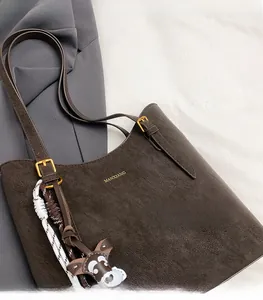 Close-up of matte coffee tote bag with gold logo and deer charm on woven strap