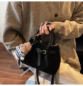 Detail of black suede bucket bag featuring a belt buckle and a cute bear charm