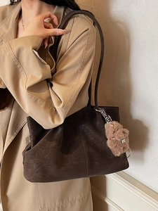 Brown faux suede tote bag with plush puppy charm on a model in a beige coat