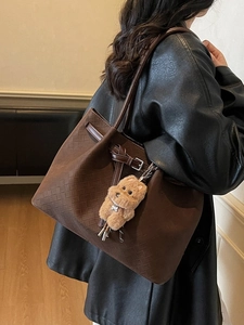 Vintage brown woven tote bag with a plush puppy charm worn by a model in a leather jacket
