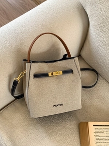 Chic beige woven bucket bag with contrast leather straps and golden swivel lock on a sofa