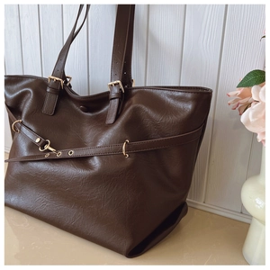 Dettaglio della borsa tote marrone scuro con texture in pelle e fibbie dorate