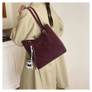 Detail of burgundy leather tote bag with a small dog charm and gold brand logo