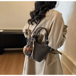 Detail of dark brown leather bucket bag with star pendant and tassel on a khaki coat