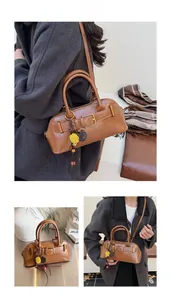 Brown faux leather shoulder bag featuring decorative buckles and a floral charm detail