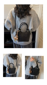 Detail of a black matte bucket bag with double handles and a brown plush bear charm