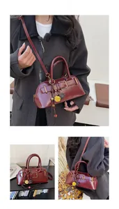 Detail of burgundy glossy shell bag with metal buckle and decorative floral pom-poms
