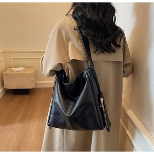 Detail of minimalist black leather tote bag with gold zipper pouch on a beige trench coat