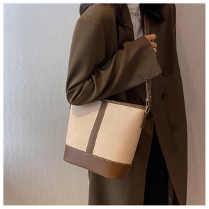Side view of beige canvas bucket bag with brown leather trim worn by model on shoulder