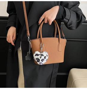 Brown litchi grain bucket bag with leopard heart charm held by a model in a black coat