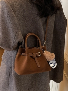 Brown faux suede bucket bag with decorative buckle and bear charm on tweed coat model
