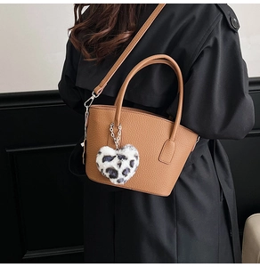 Detail of a brown leather tote with a stylish leopard heart pendant on a dark coat