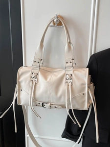 Sac à main rétro crème en similicuir avec pompons et rivets argentés contre un mur blanc