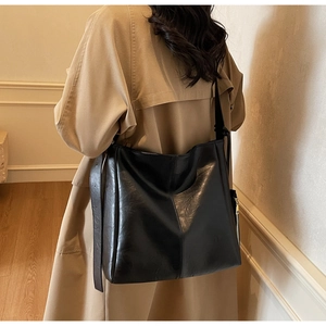 Detail view of large black leather tote bag with vertical seams on a khaki coat