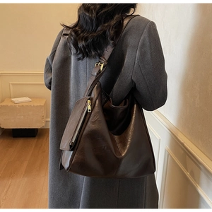 Detail of a dark brown leather tote bag with gold zipper shown on a model