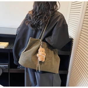 Olive green suede tote bag with white stitching and bear charm on model's shoulder
