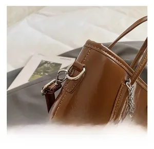 Close-up of brown bucket bag with metal hook buckle and detailed stitching on glossy leather