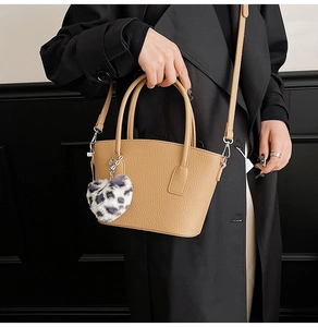 Detail of camel brown leather bucket bag with leopard heart charm on a black coat