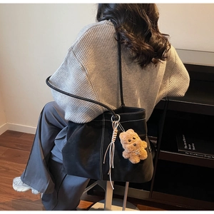 Detail of black tote bag with white contrast stitching, bear charm, and leather tassel