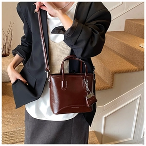 Detail of dark brown glossy leather bucket bag with short handles and shoulder strap