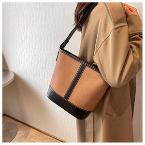 Detail of canvas bucket bag with black leather trim and white contrast stitching on model