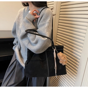 Detail of black suede tote bag with white contrast stitching and bear charm